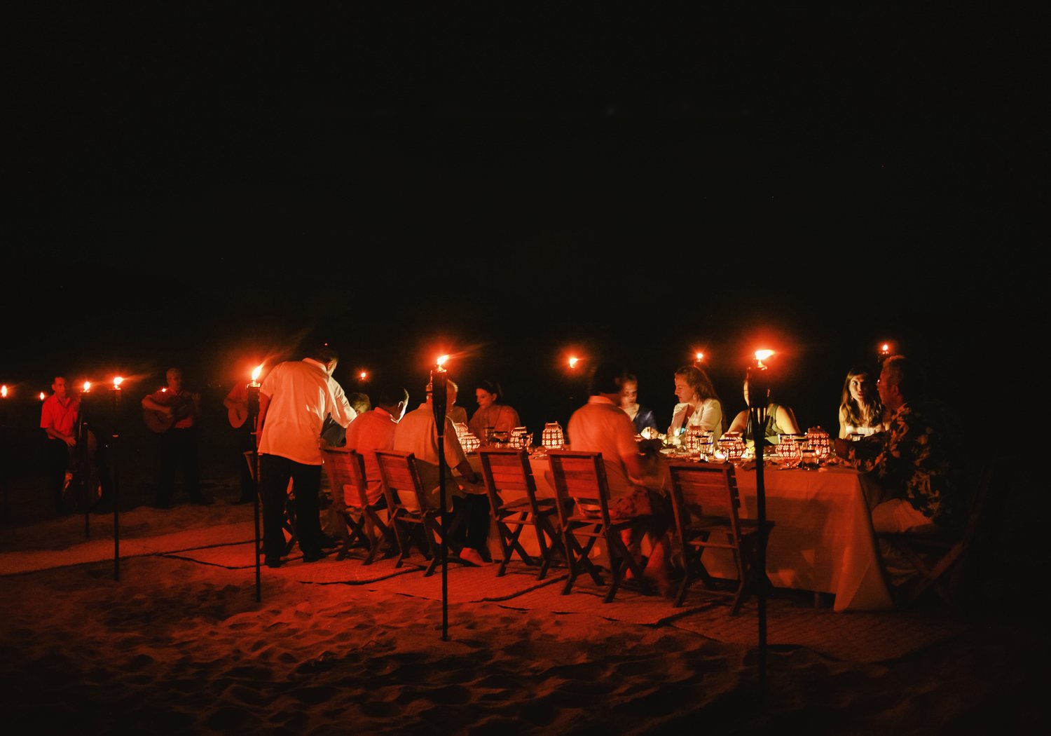 A private dinner on the beach: a long table on the sand lit by torches at night