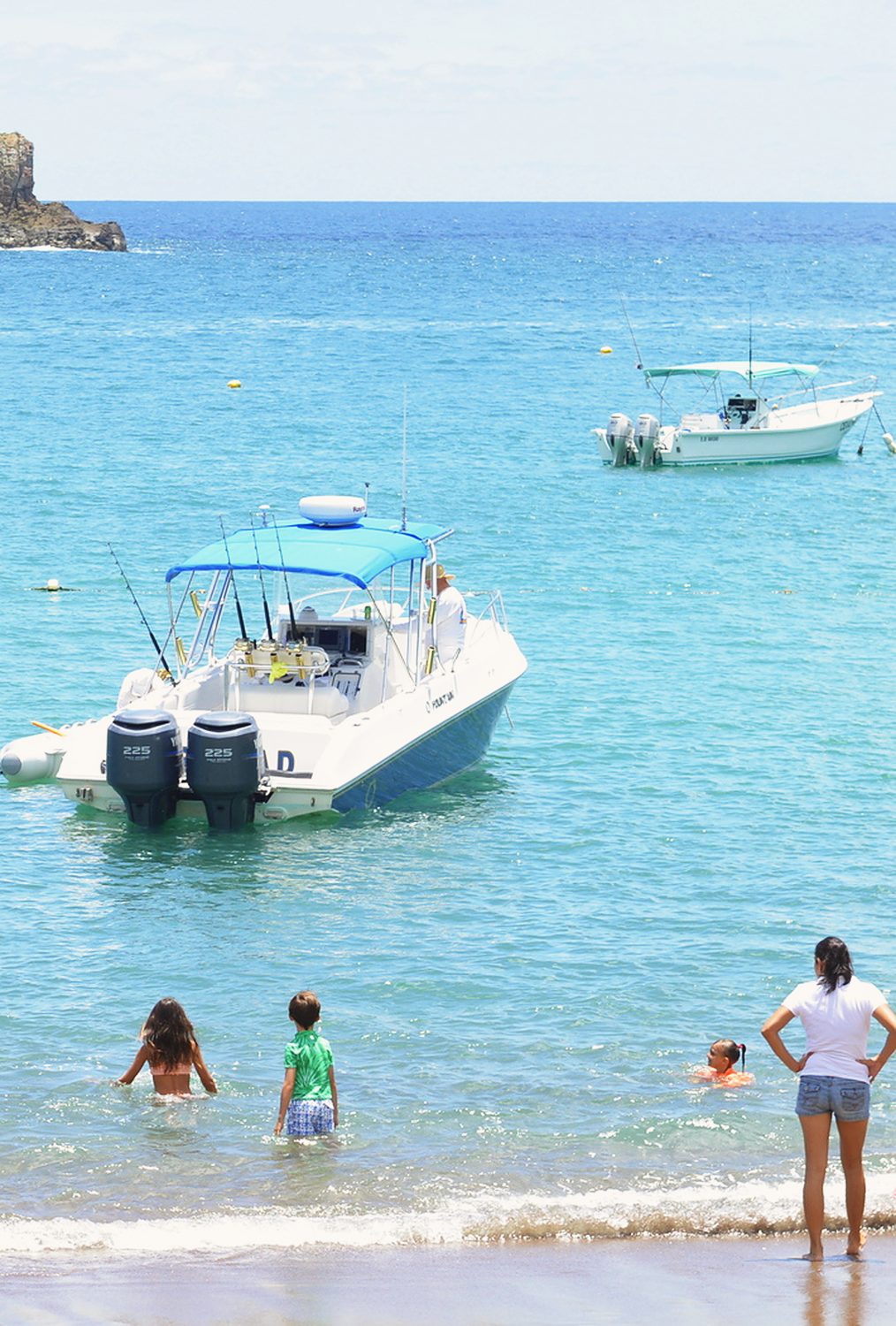 Motor boat anchored in a turquoise bay with swimmers wading in from the beach