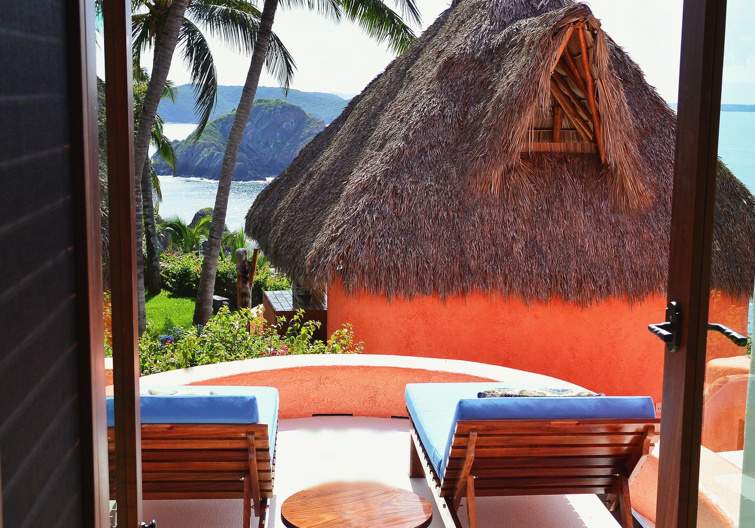 The Emerald private patio: two blue-cushioned loungers and a thatched casita seen through open doors, with the bay beyond