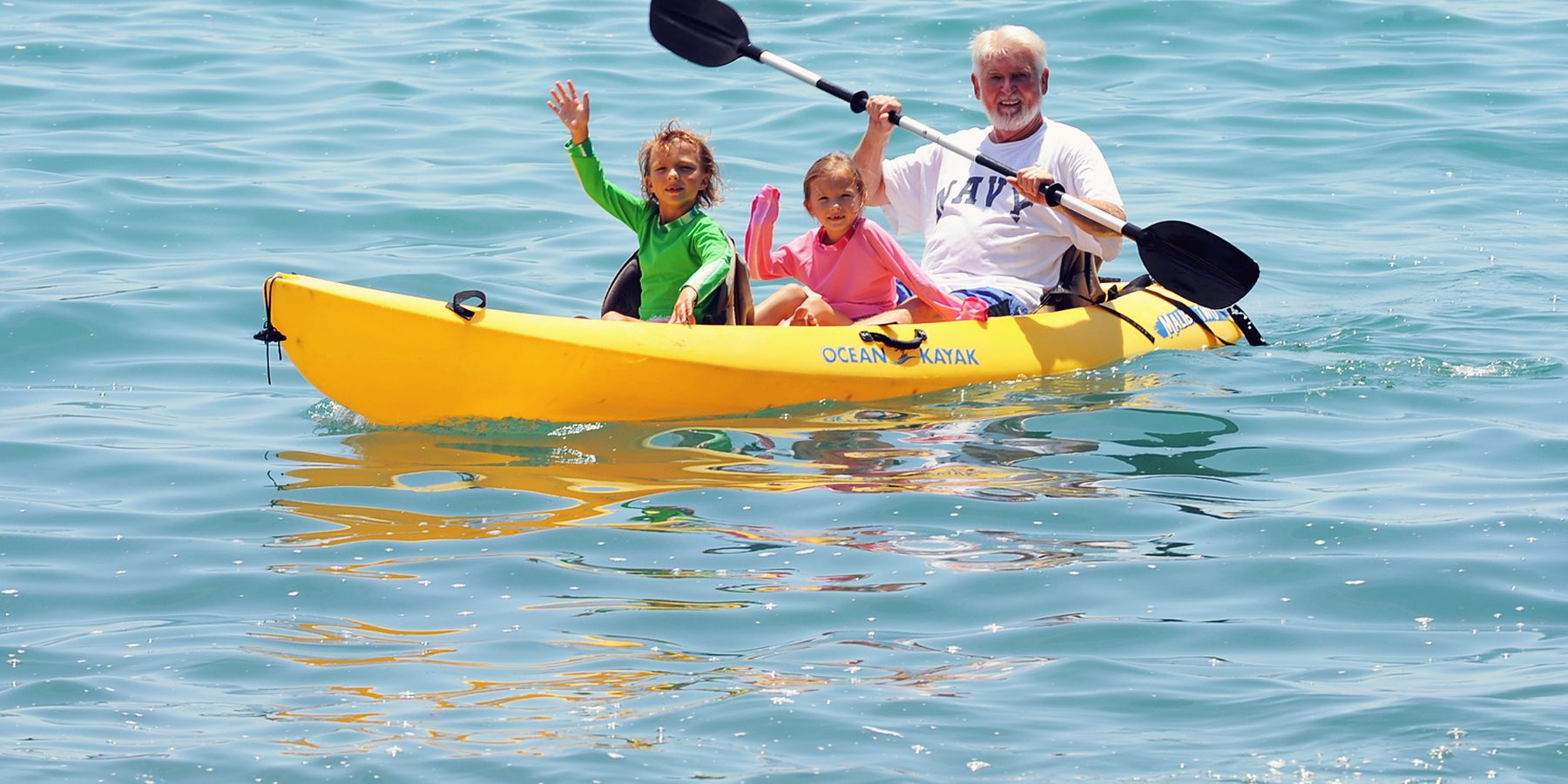 A family paddling a yellow kayak in turquoise water