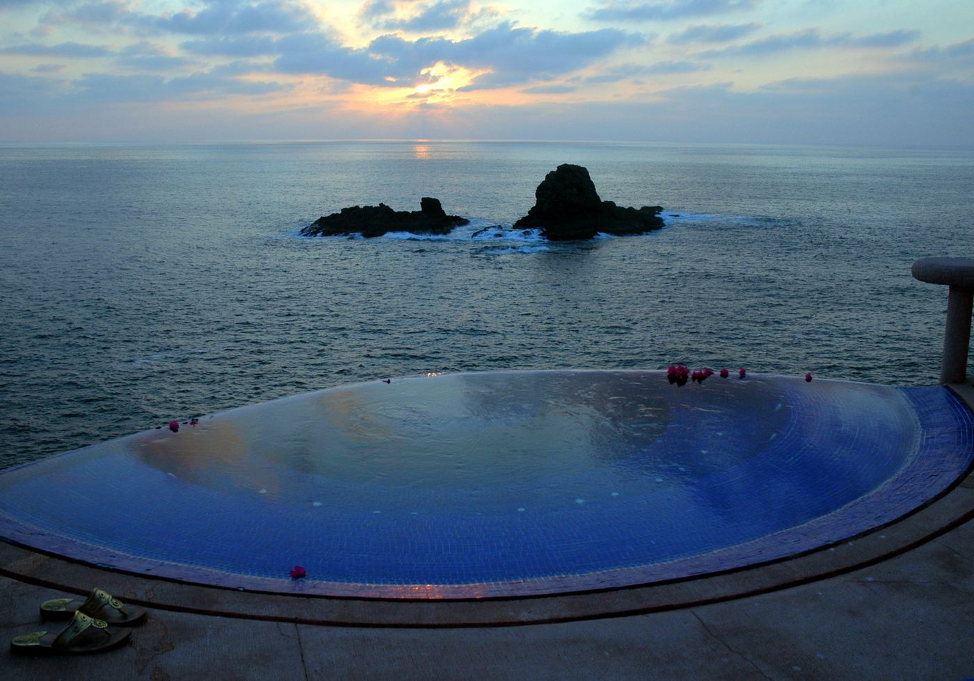 The jacuzzi at sunset, with soft clouds reflected and two rocks in the darkening sea beyond