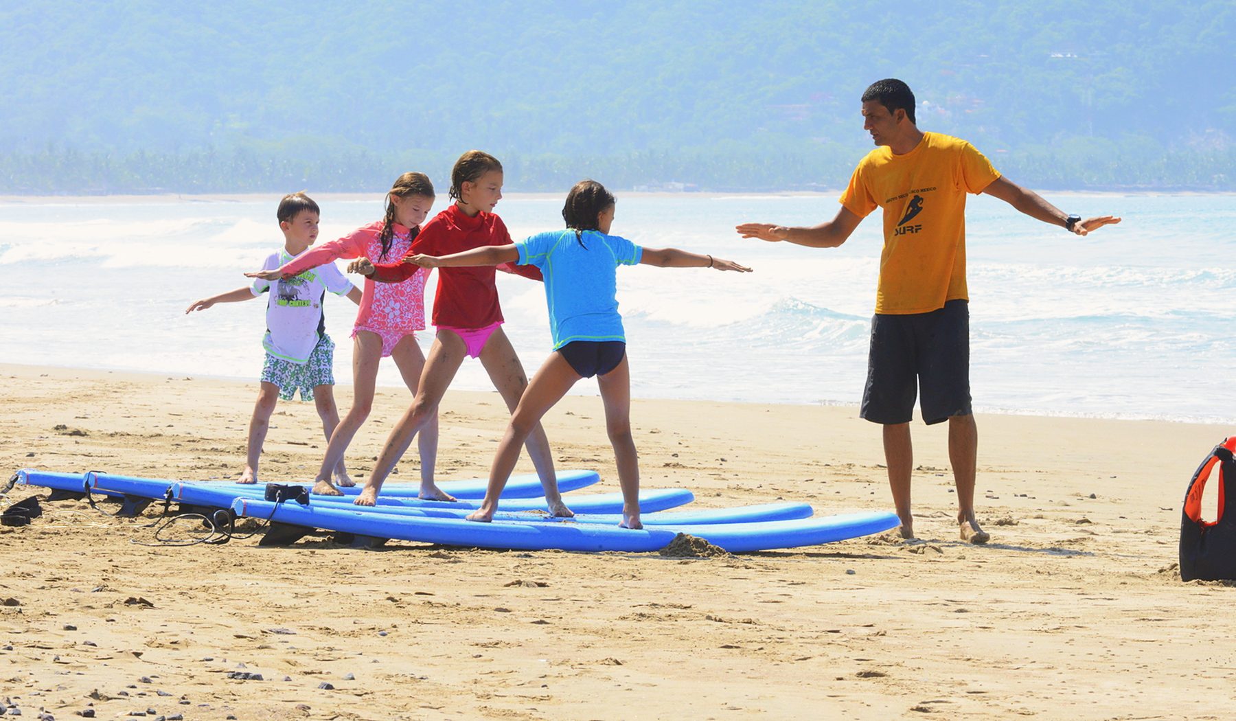 Children learning to stand on blue surfboards on the beach with a surf instructor